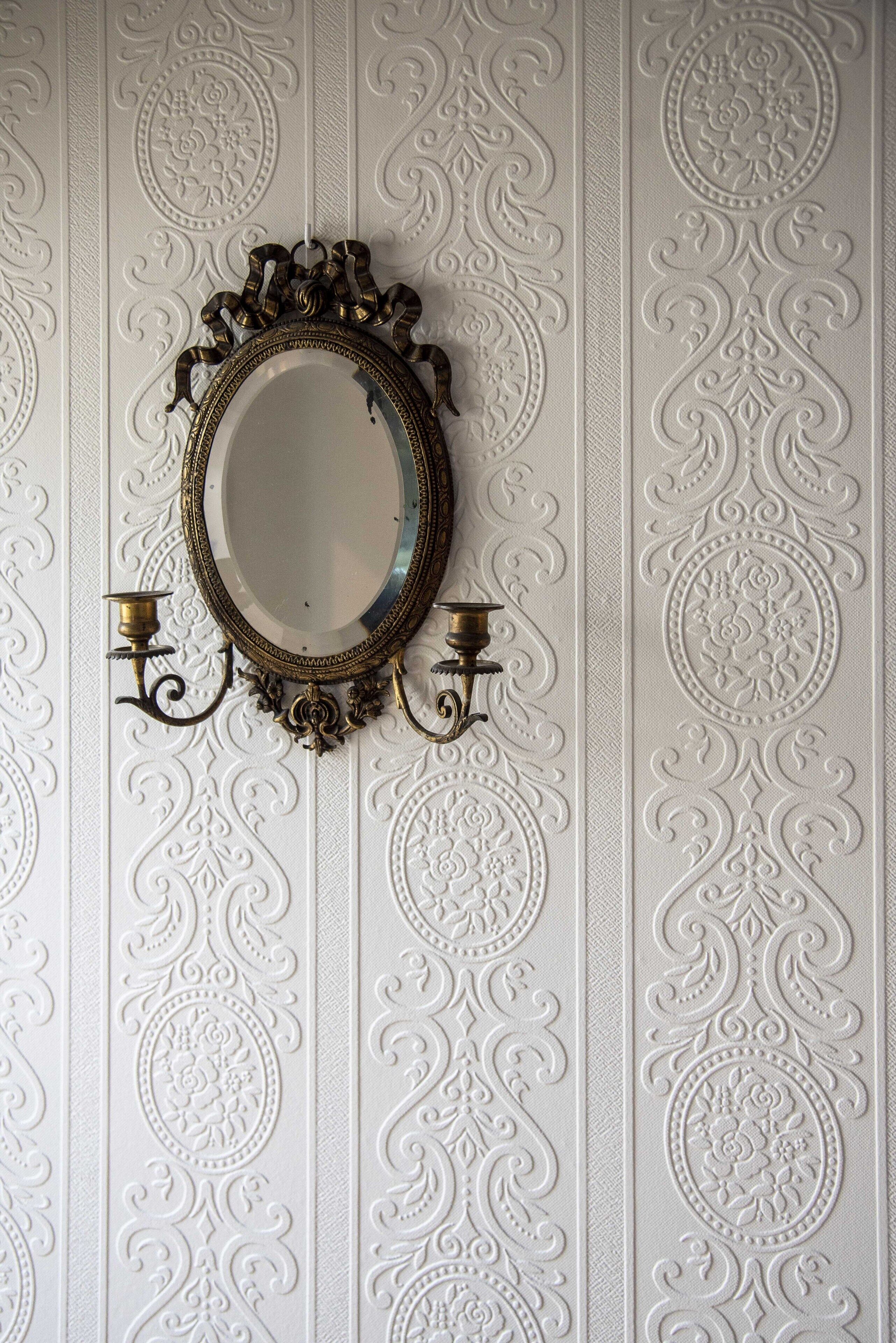 A wall with ornate, embossed patterns and a decorative mirror with two candle sconces.