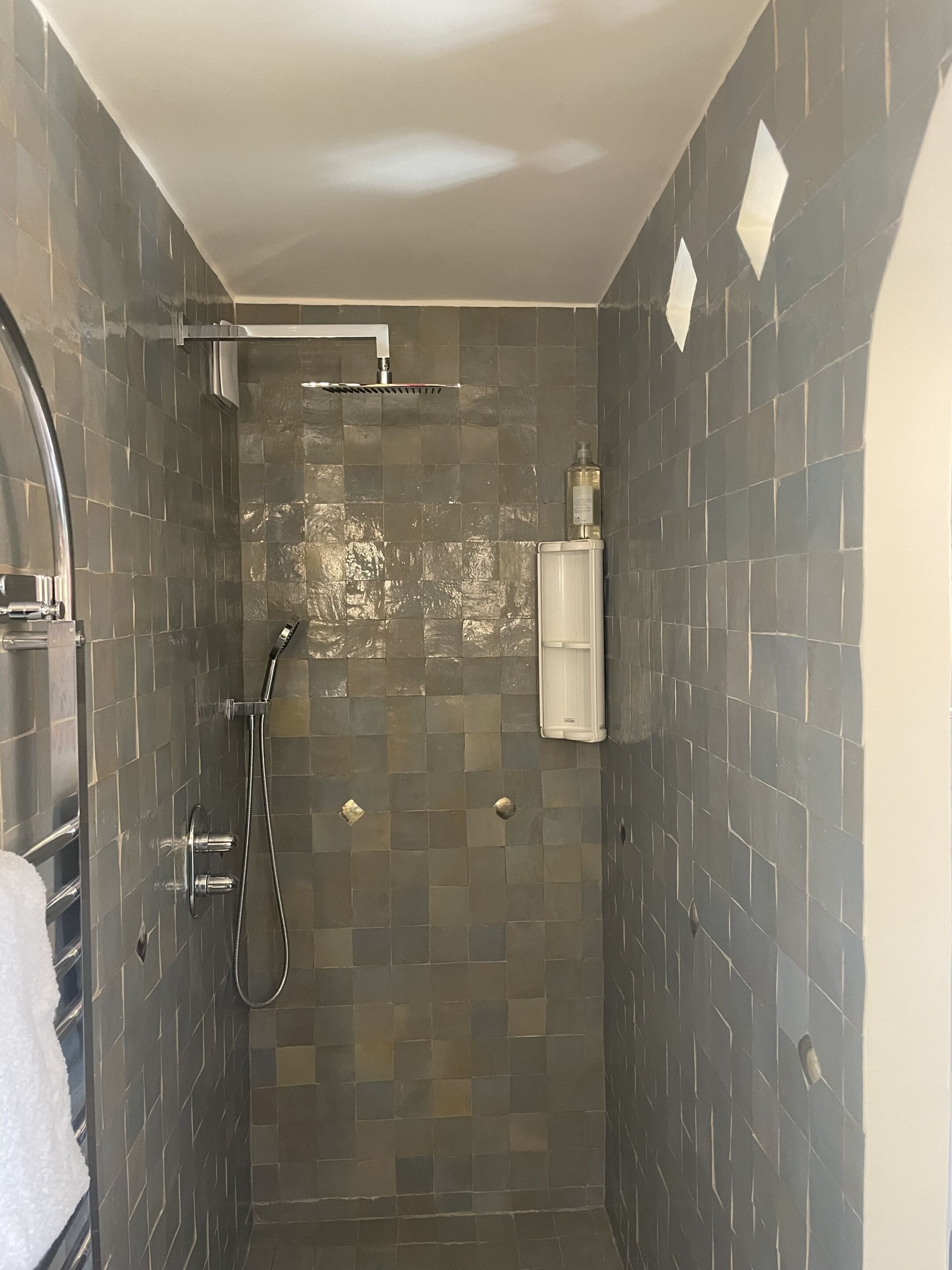 Un baño pequeño con azulejos, un cabezal de ducha manual y un grifo empotrado en la pared.