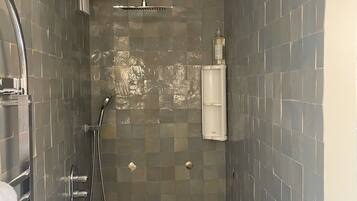 Un baño pequeño con azulejos, un cabezal de ducha manual y un grifo empotrado en la pared.
