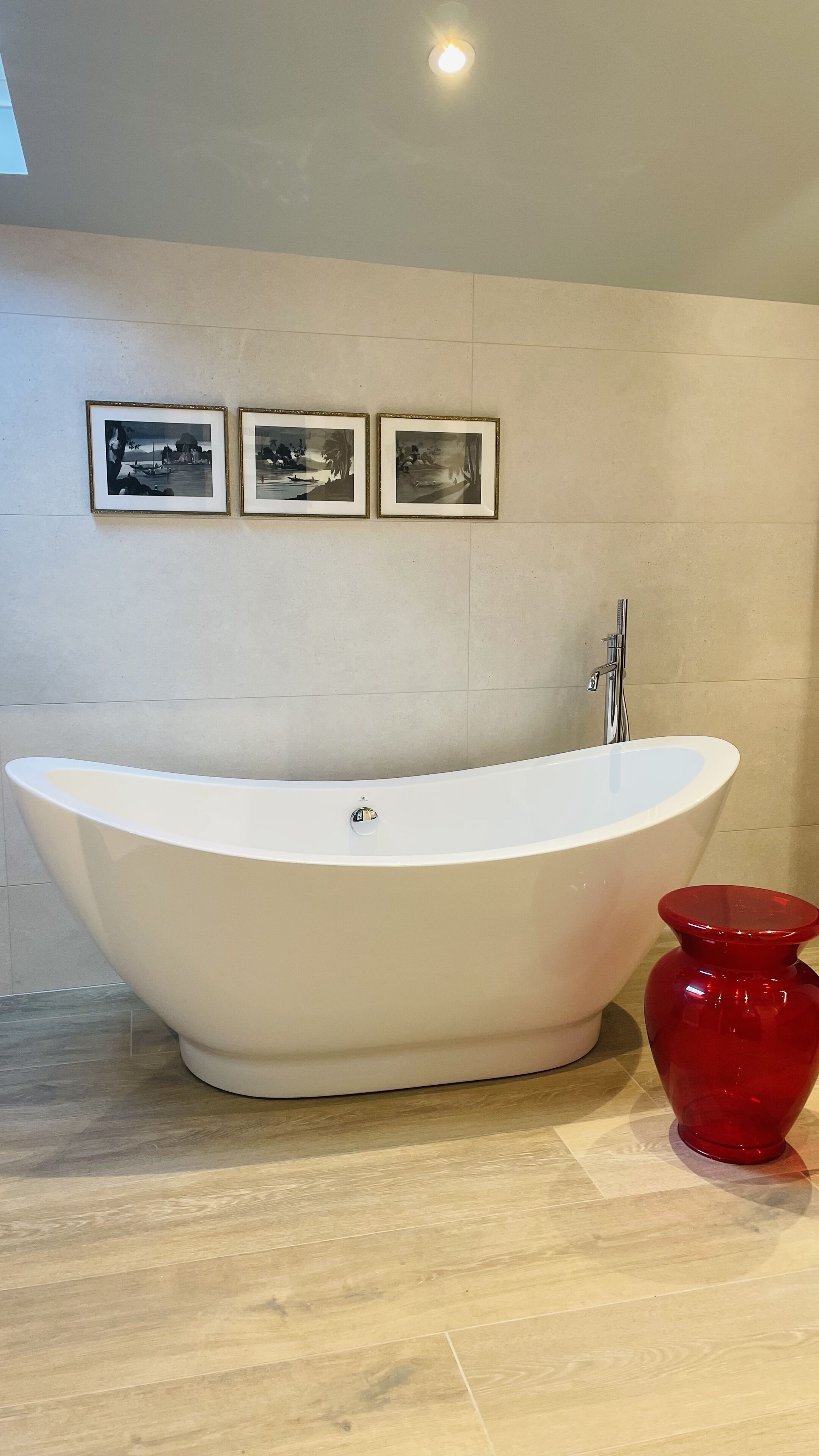 A modern bathroom with a freestanding bathtub, a red vase, and three framed pictures on the wall.