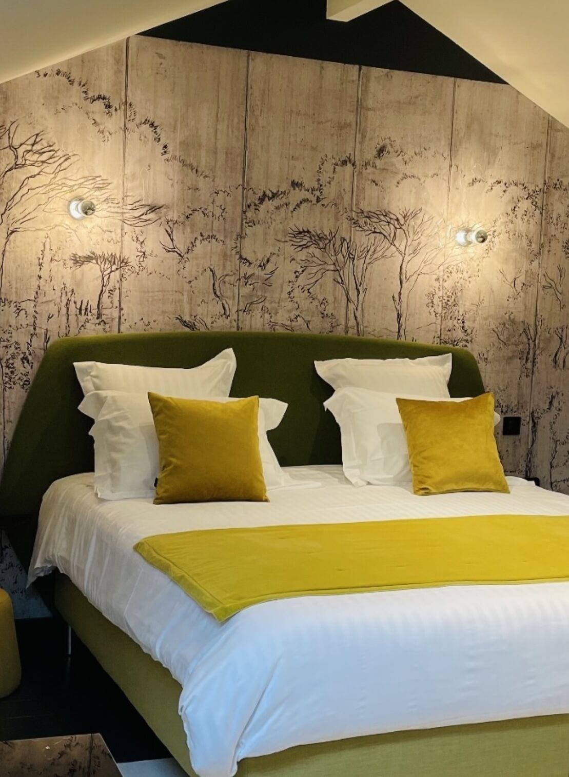 A bed with white and yellow bedding, a green headboard, and a wooden wall with tree designs.