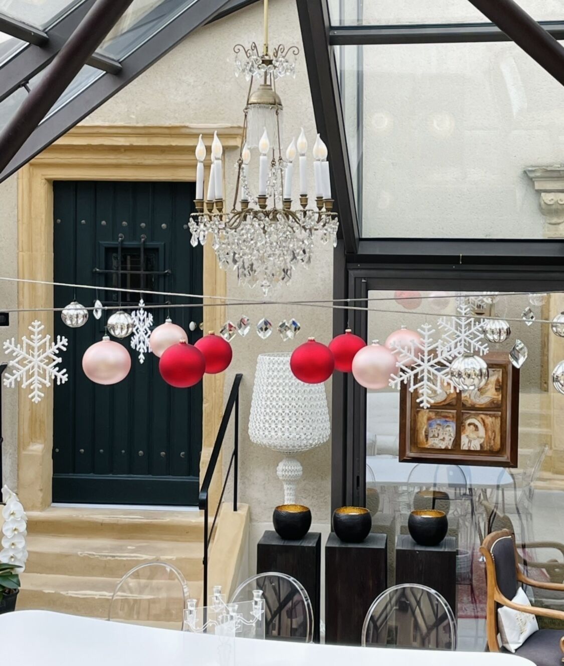 Uma sala de jantar com um candelabro, decorações de Natal e vista para a rua.
