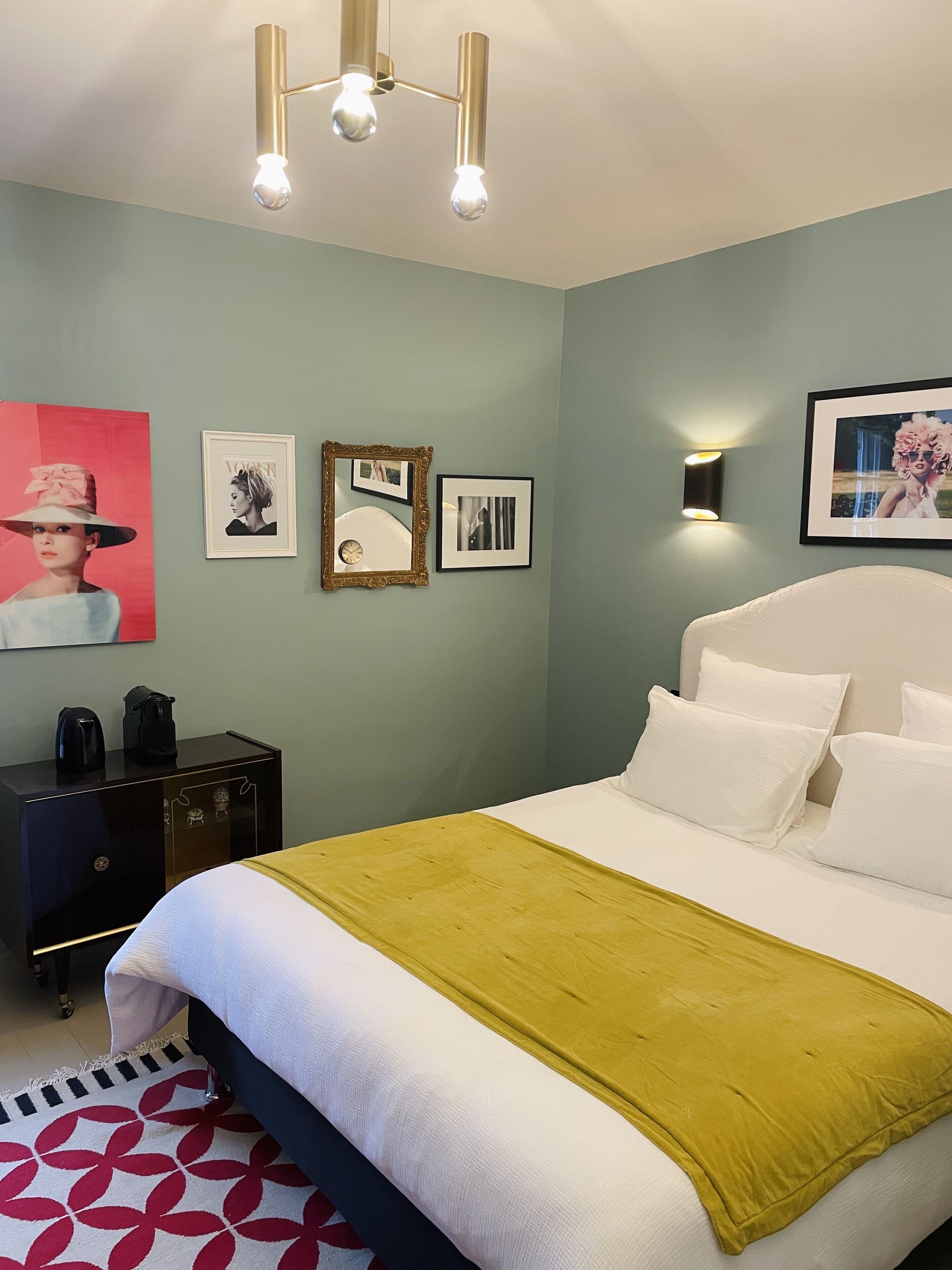 Un dormitorio ordenado con cama, mesitas de noche, una lámpara de pared y cuadros enmarcados.