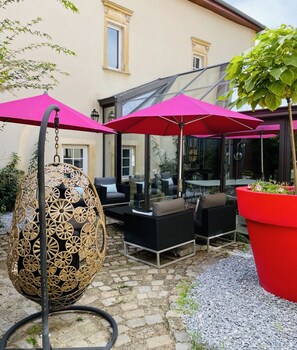 A patio with wicker furniture, red umbrellas, and a hanging chair. - La Maison Ruffinoise (Sainte-Ruffine)
