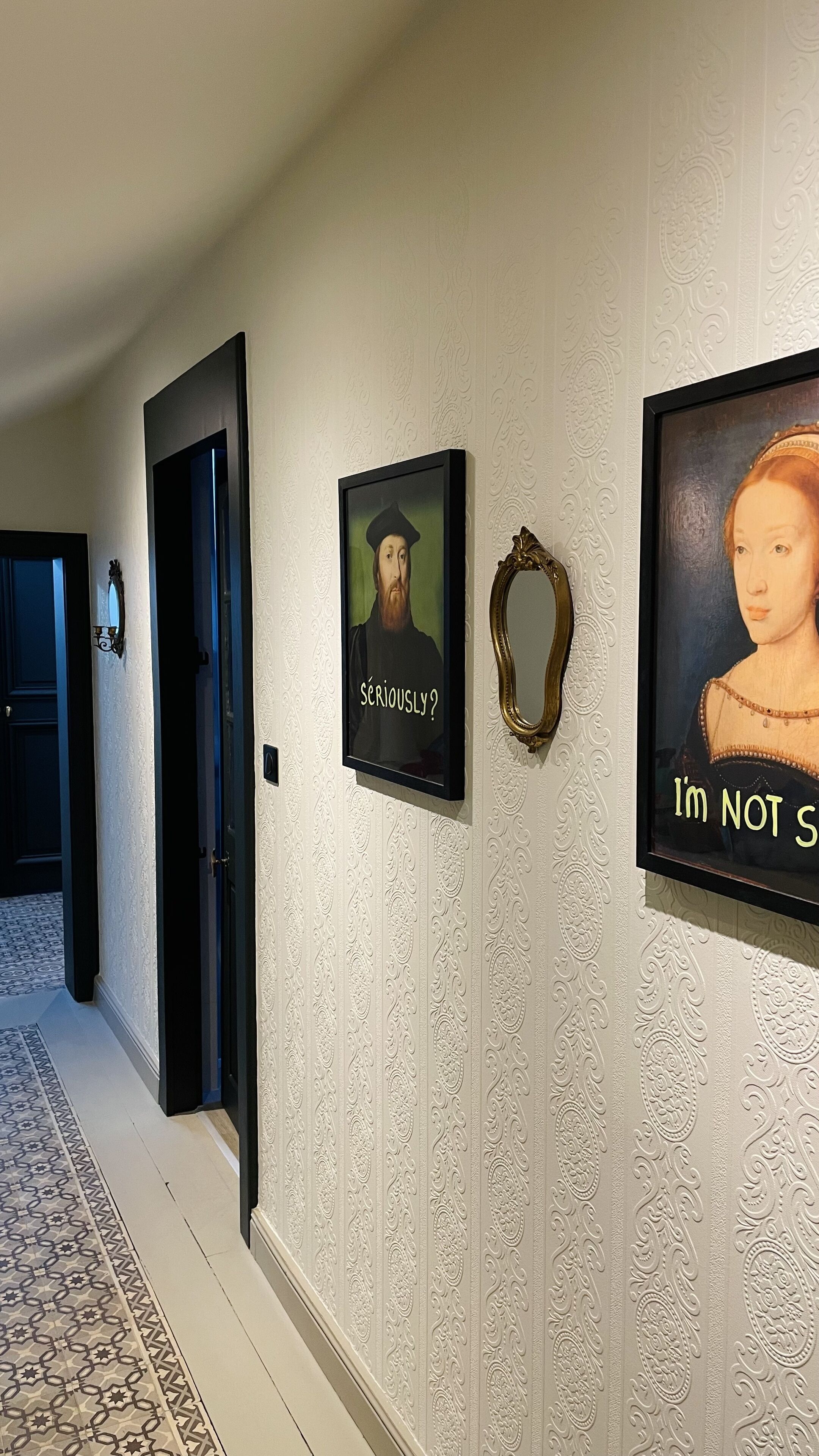 Een gang met behang met een patroon, ingelijste kunstwerken en een decoratieve spiegel.