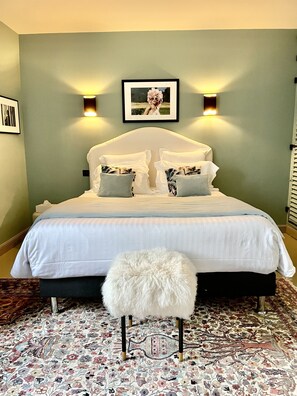 A neatly made bed with white linens and two pillows, a fluffy white stool, and a patterned rug on the floor. - La Maison Ruffinoise (Sainte-Ruffine)