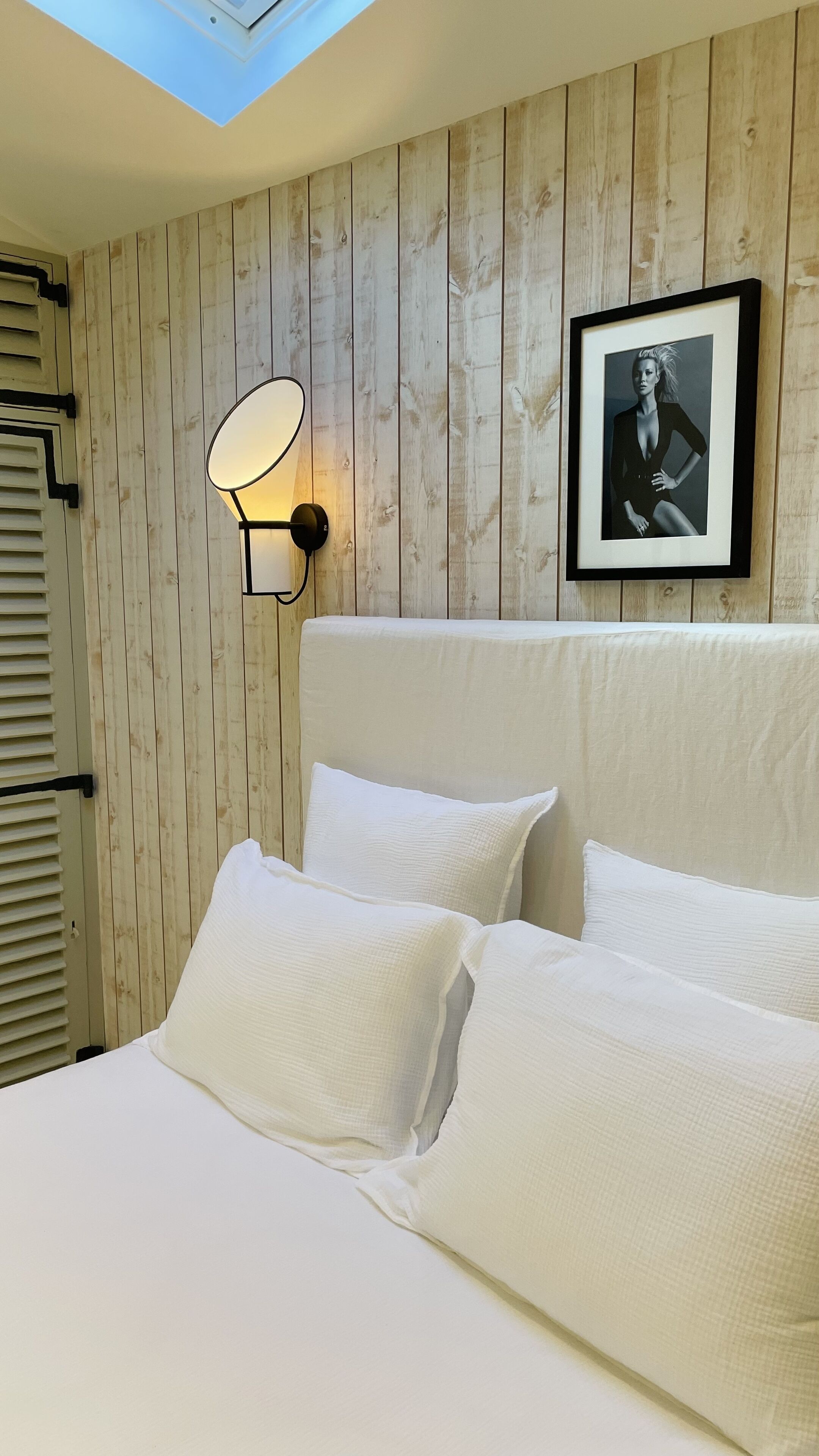 A bedroom with a wooden wall, a framed picture, and a bed with white bedding.