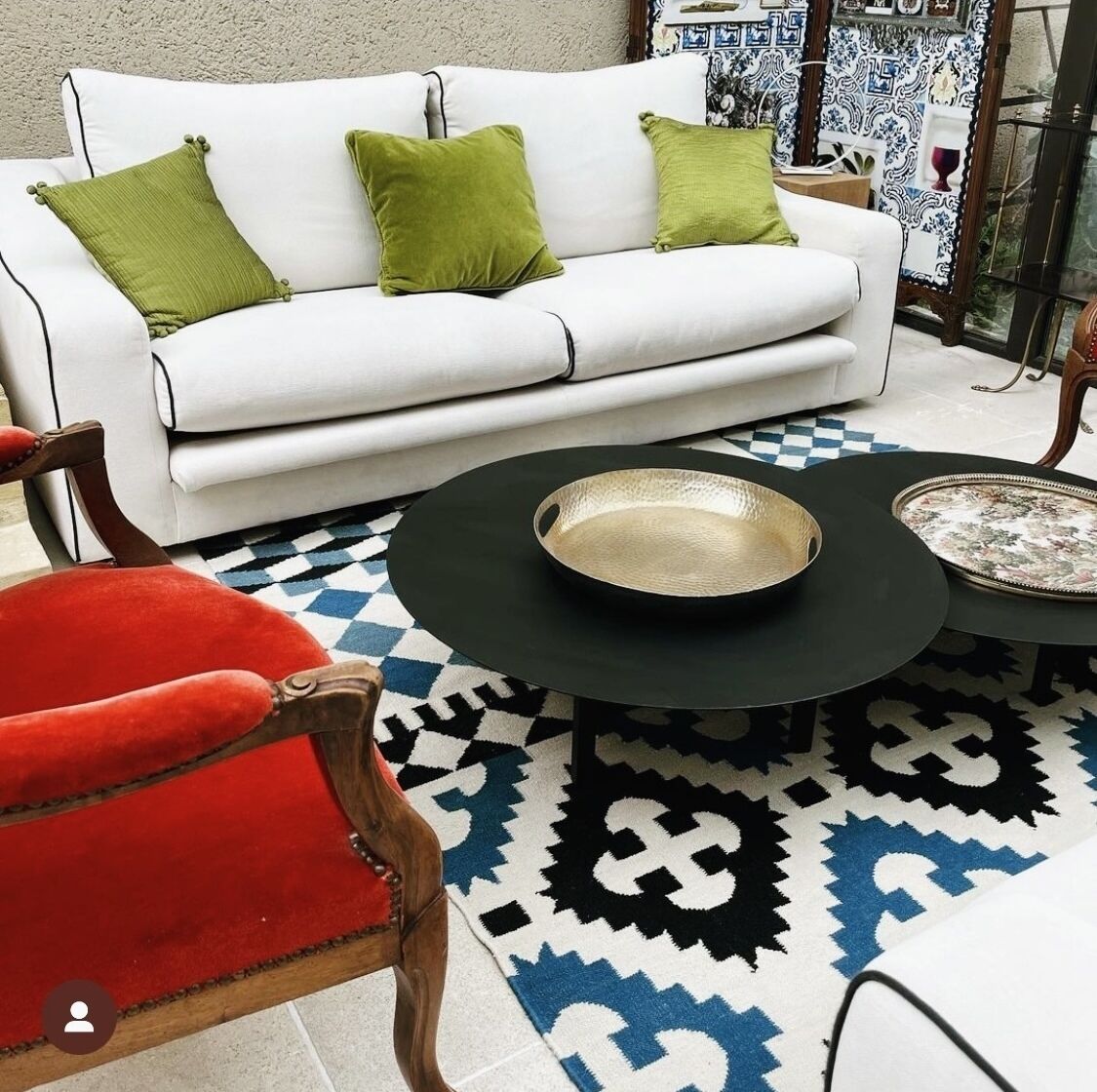 A white sofa with green cushions, a red chair, and a black coffee table with a bowl and tray.