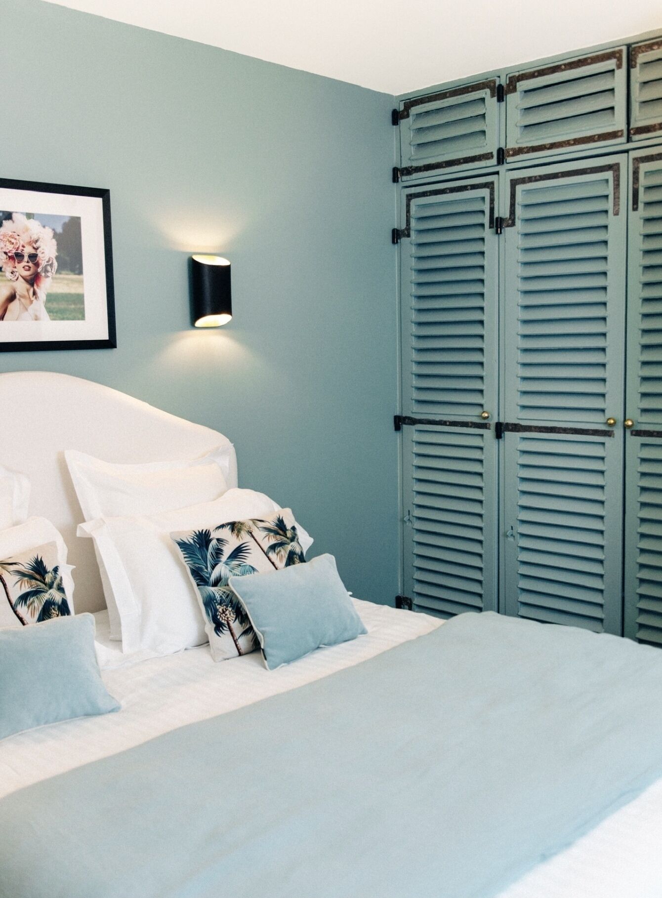 Een slaapkamer met een bed, kussens, een wandlamp en een kledingkast.