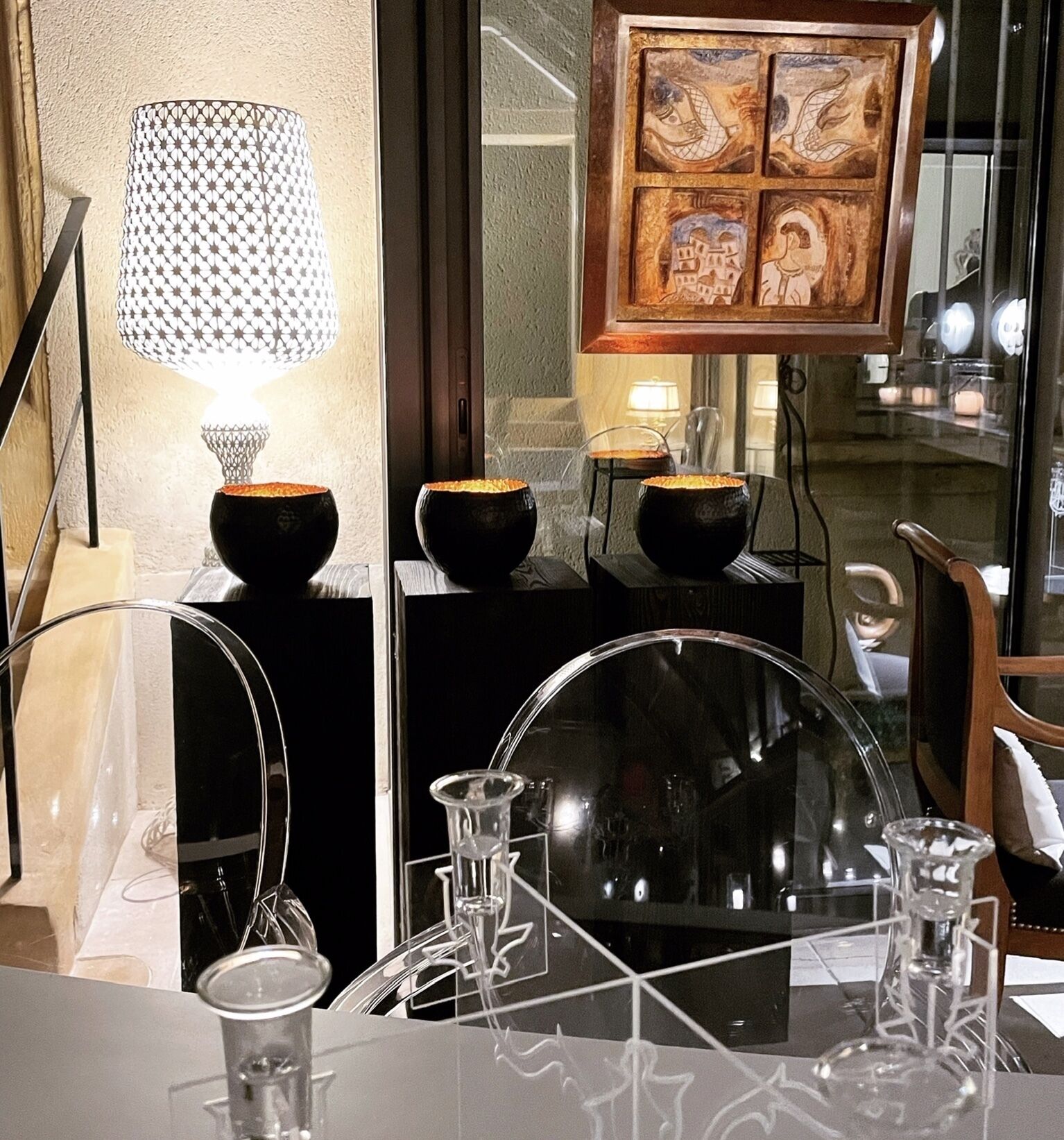 A modern dining area with a glass table, black bowls, and a decorative lamp.