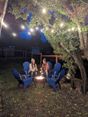 An outdoor seating area with chairs around a fire pit, under string lights.