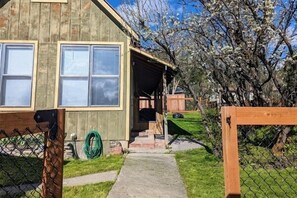 A wooden house with a porch, a fenced yard, and a tree with white blossoms.
