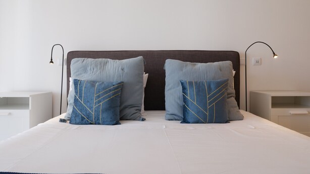 Een net opgemaakt bed met twee kussens, een hoofdbord, nachtkastjes en wandlampen.