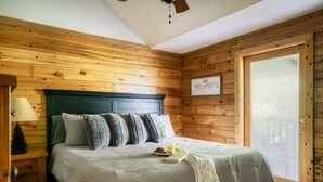 Une chambre à coucher aux murs lambrissés, comprenant un lit, une table de chevet, une lampe et une fenêtre donnant sur une terrasse.