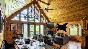 L’intérieur d’un chalet en bois comprend un coin repas, une cheminée et une tête d’animal empaillée accrochée au mur.