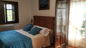 Quarto com cama, janela, radiador e porta que dá para área externa.