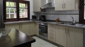 Cozinha com armários de madeira clara, micro-ondas, fogão e janela com vista para vegetação.