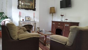 Uma sala de estar com duas poltronas, lareira, televisão e estante de livros.