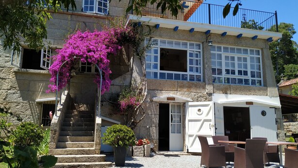 Edifício de pedra com escadaria, área de estar coberta ao ar livre e uma RV branca estacionada na frente.