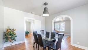 Un espace repas avec une table en verre et des chaises noires, un luminaire au plafond et un plancher en bois.