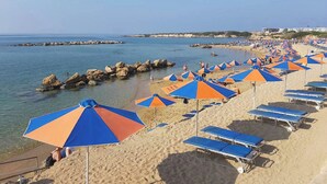 Una playa con hileras de sombrillas azules y anaranjadas, y sillas de baño.