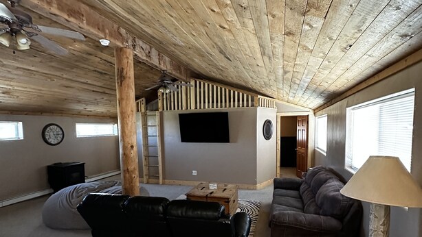 Un vaste espace de vie doté d’un haut plafond, de poutres en bois, d’un canapé en cuir noir, d’un divan marron, d’une lampe et d’un téléviseur.