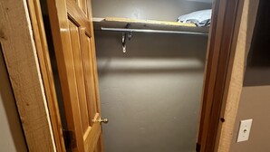 Un couloir étroit, avec une porte en bois sur la gauche et un placard avec une tringle en métal sur la droite.
