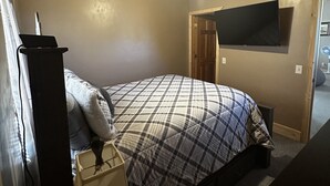 Une chambre à coucher avec un lit, un bureau, une lampe, un téléviseur et un ventilateur de plafond.