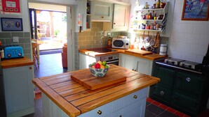 A kitchen with a wooden countertop, a microwave, and a bowl of fruit. There are cabinets and a stove in the background.