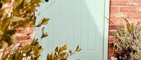 A light blue door with a small window and a bell above it. There is a sign above the door that reads 'Orchard Cottage.'