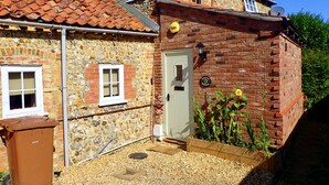 A stone house with a red-tiled roof, a white door, and a small garden with plants.