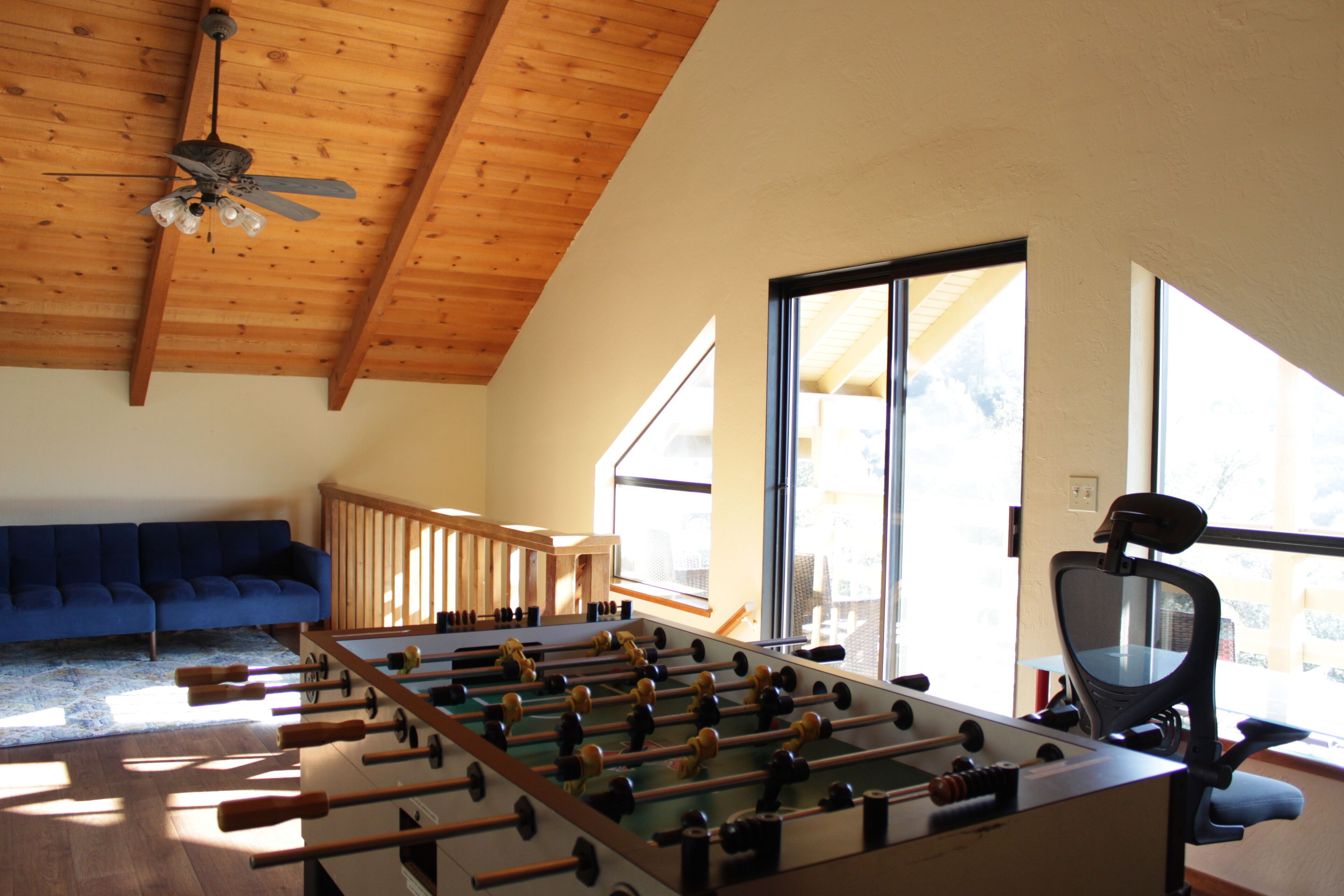 A room with a foosball table, a blue sofa, and a window providing natural light.