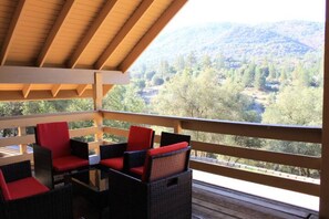A covered outdoor seating area with wicker chairs and red cushions, overlooking a mountainous landscape. - Beach/river access, A/C in every room, mountain view, games, family friendly (Oakhurst)