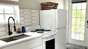 Een keuken met witte kasten, een gasfornuis, een inbouwoven, een koelkast en een raam met jaloezieën.