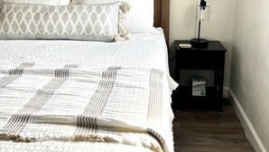 Een net opgemaakt bed met beddengoed met een patroon, een houten hoofdbord en een nachtkastje met een lamp.