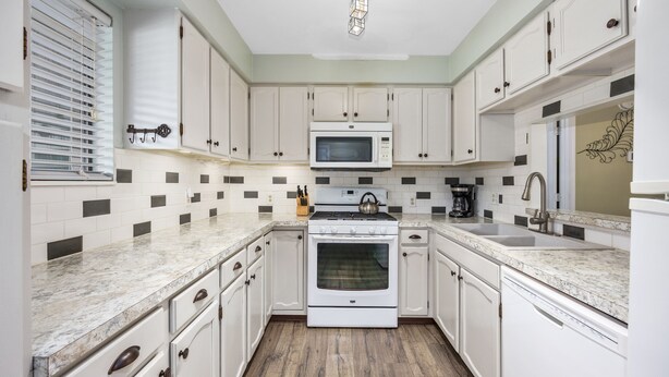 A kitchen with white cabinets, a microwave, an oven, and a sink.