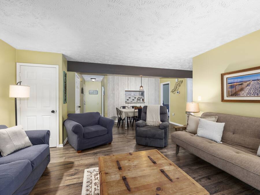 Una sala de estar con un sofá, sillones, una mesa de centro y un comedor al fondo.