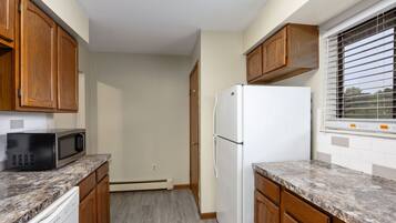 A kitchen with wooden cabinets, a white refrigerator, a microwave, and a window with blinds.