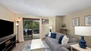 A living room with a flat-screen TV, a grey sofa, a white coffee table, and a blue lamp.