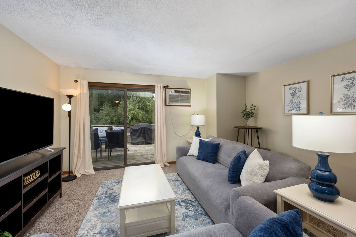 A living room with a flat-screen TV, a grey sofa, a white coffee table, and a blue lamp.
