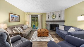 A living room with a fireplace, a sofa set, a wooden coffee table, and a large window with curtains.