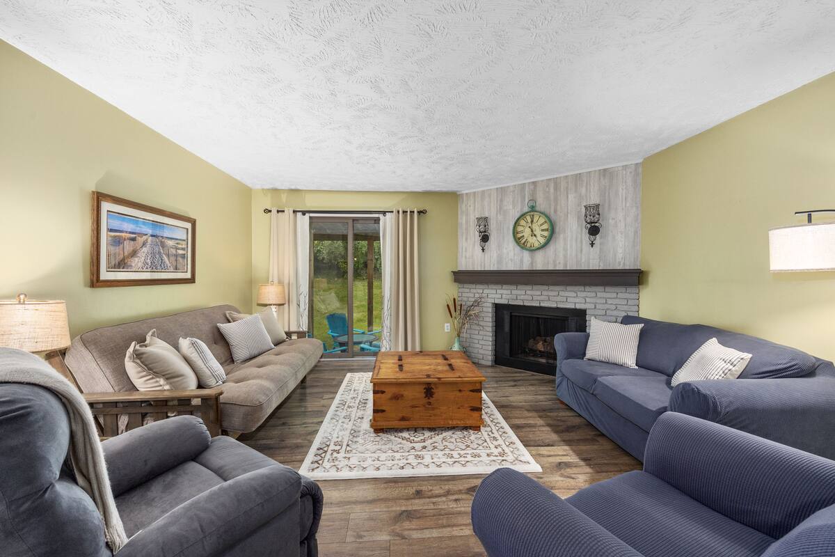 A living room with a fireplace, a sofa set, a wooden coffee table, and a large window with curtains.