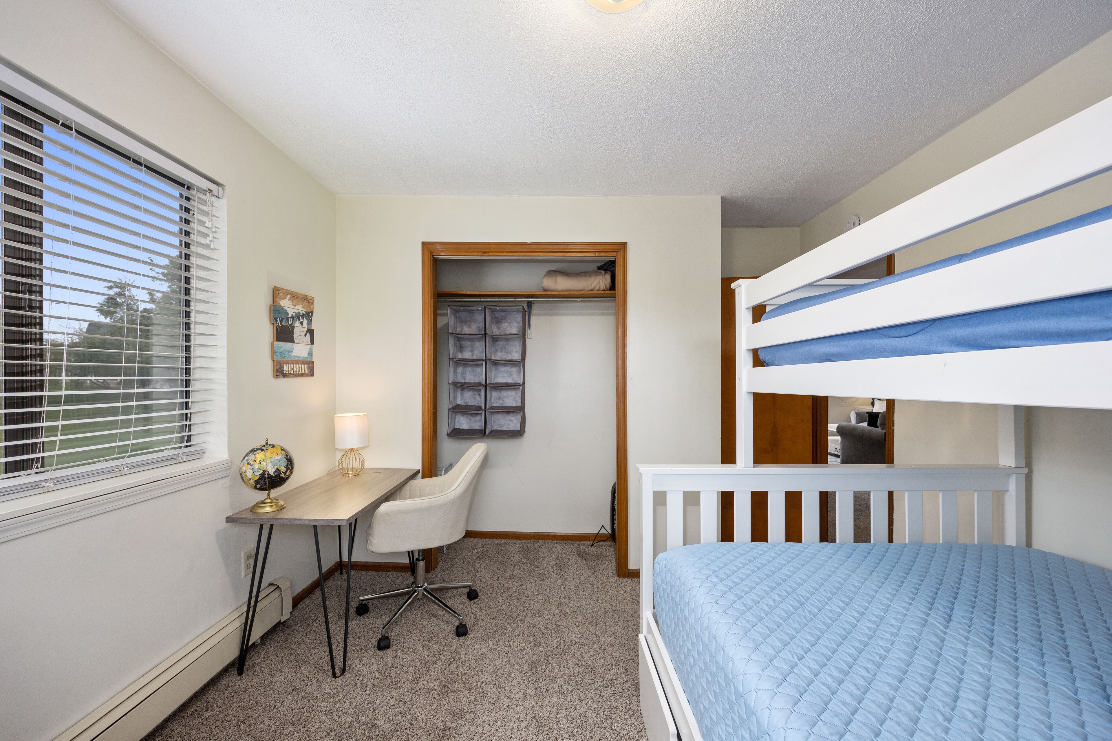 A bedroom with bunk beds, a desk with a chair, a globe, and a closet with hanging clothes.