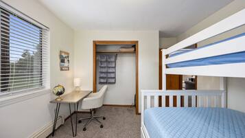 A bedroom with bunk beds, a desk with a chair, a globe, and a closet with hanging clothes.