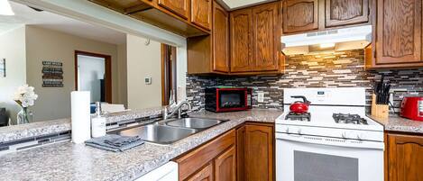 A kitchen with wooden cabinets, granite countertops, a microwave, a stove, and a sink.