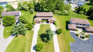 An aerial view of a residential area with multiple houses, a central driveway, and surrounding greenery.