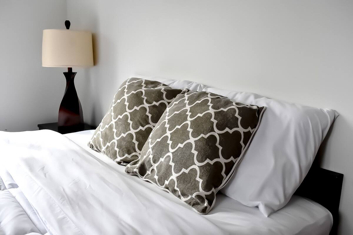A neatly made bed with white bedding and two patterned pillows.
