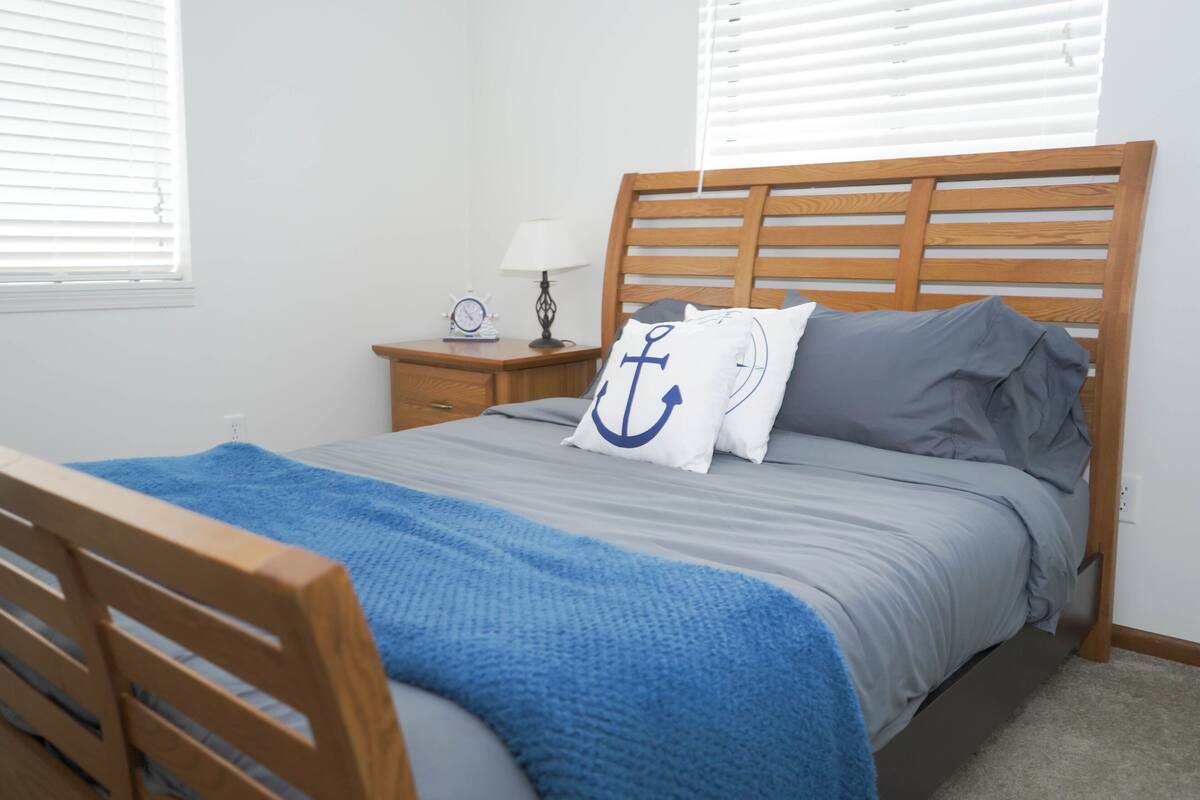 A neatly made bed with a blue blanket, a wooden headboard, and pillows with a blue anchor design.