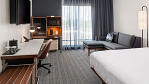 Habitación de hotel con cama, escritorio con computadora, sofá, televisión montada en la pared, microondas y lámpara.