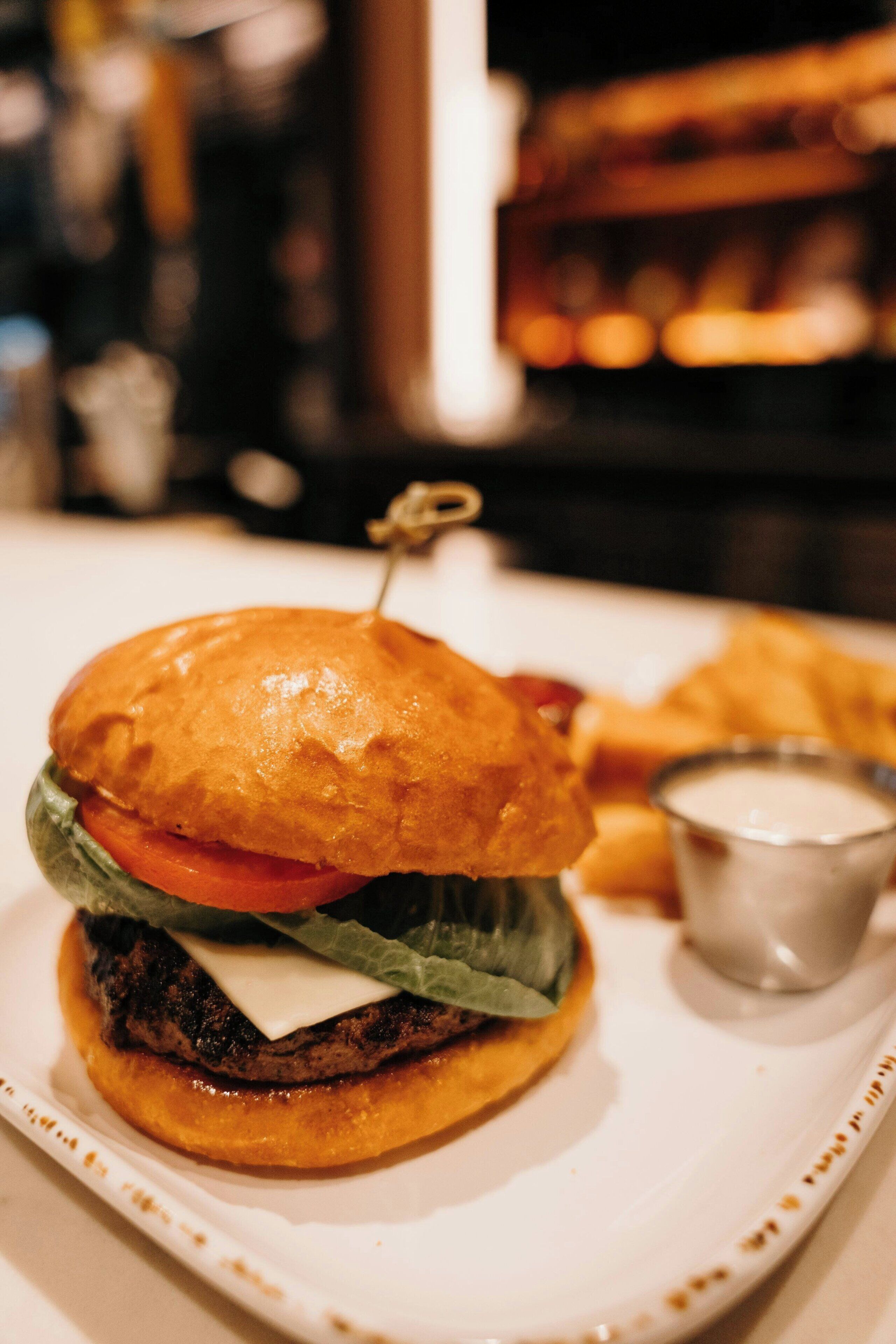 Ein Burger mit Zahnstocher auf einem weißen Teller, dazu eine kleine Servierschale für Dip.